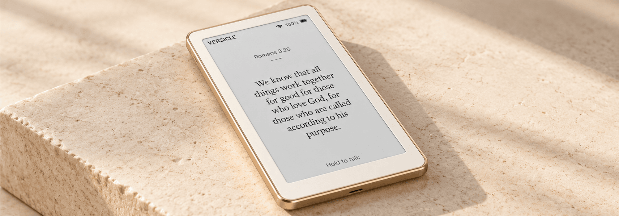 A gold-edged Versicle displaying Romans 8:28 and Hold to talk on a sunlit stone surface